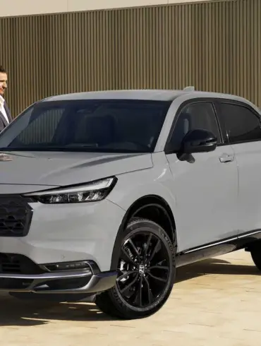 Honda HR-V e:HEV in Grau mit schwarzem Grill, geparkt vor moderner Architektur, zwei Personen daneben.