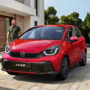 Honda Jazz e:HEV in roter Lackierung steht auf einer Einfahrt vor einem modernen Haus, daneben ein Mann.