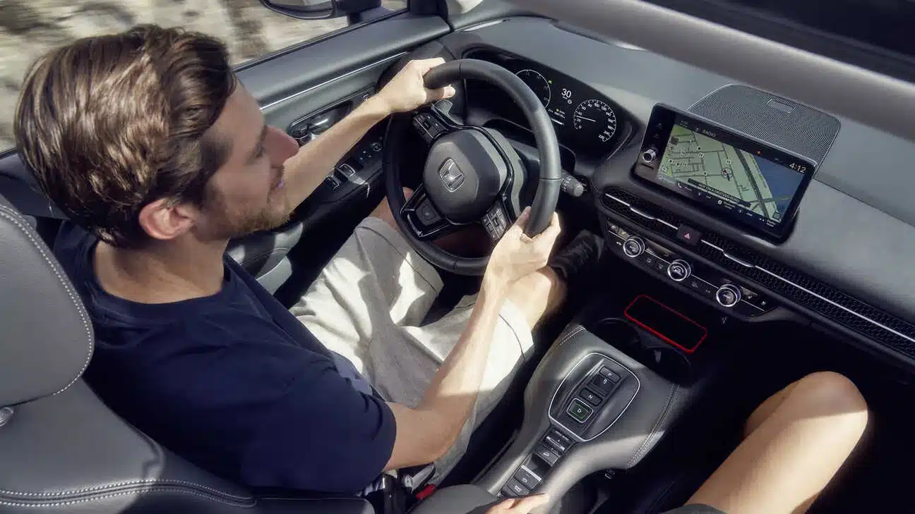 Innenraumansicht eines fahrenden Honda ZR-V e:HEV mit Fokus auf Lenkrad, Infotainmentsystem und Armaturenbrett.