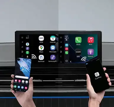 Infotainmentsystem des KGM Musso Grand mit Apple CarPlay und Android Auto, zwei Hände halten Smartphones vor dem Display.