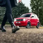 Roter Ligier Myli MAX auf der Straße, vorne schwarze 14-Zoll-Leichtmetallfelgen, Person im Vordergrund geht vorbei.