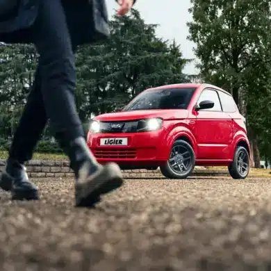 Roter Ligier Myli MAX auf der Straße, vorne schwarze 14-Zoll-Leichtmetallfelgen, Person im Vordergrund geht vorbei.
