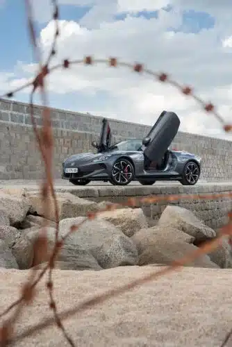 MG Cyberster Roadster mit geöffneten Scherentüren vor einer Steinmauer und Felsen, aufgenommen bei Tageslicht