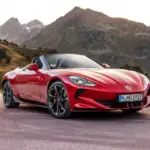 Roter MG Cyberster Roadster steht vor Berglandschaft mit offenem Verdeck.