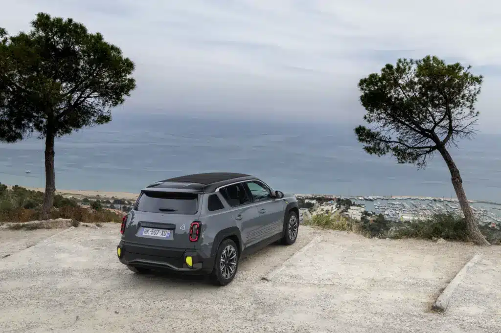 Renault 4 E-Tech elektrisch Plein Sud in Grau mit schwarzem Stoffdach, geparkt oberhalb eines Hafens am Meer