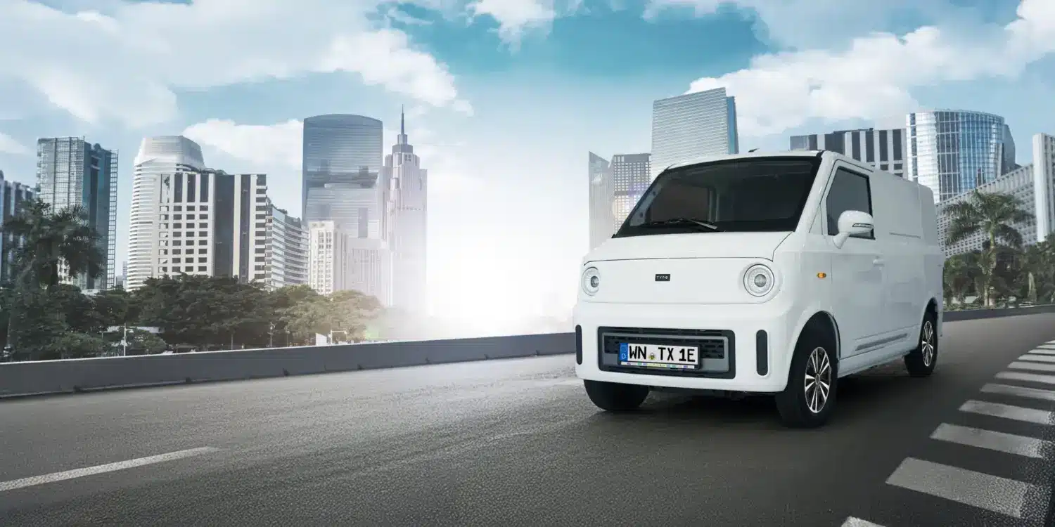 Weißer TX1-e Elektro-Transporter fährt vor moderner Skyline auf städtischer Straße.
