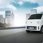 Weißer TX1-e Elektro-Transporter fährt vor moderner Skyline auf städtischer Straße.