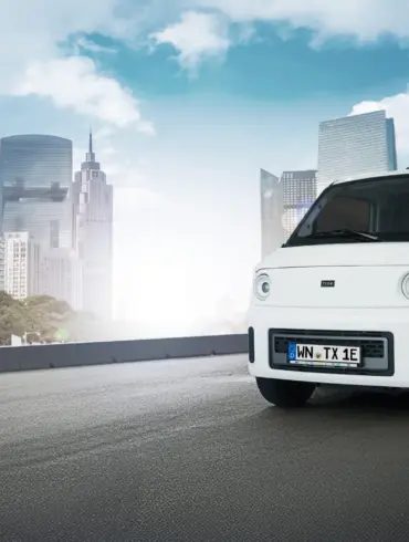Weißer TX1-e Elektro-Transporter fährt vor moderner Skyline auf städtischer Straße.