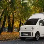 Weißer TYN-e TX7 Elektro-Transporter steht auf einer von Bäumen gesäumten Allee im Herbst.