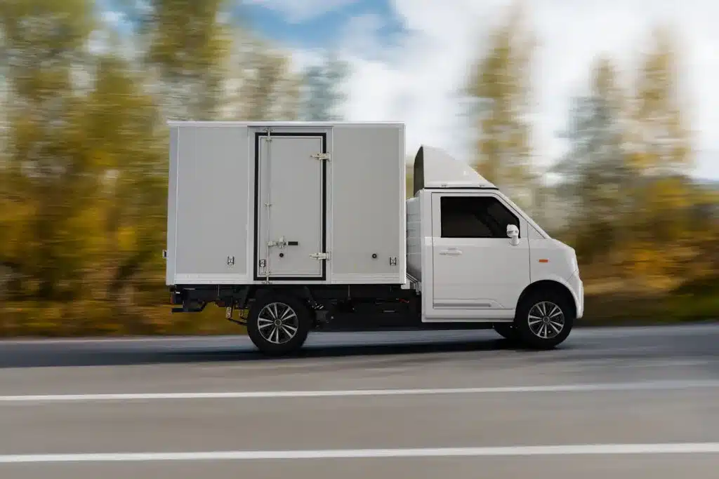 Weißer TYN-e TX7 Elektro-Transporter mit Kastenaufbau fährt auf einer Landstraße.