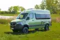 Grüner Westfalia James Cook 600 D Kastenwagen auf Mercedes Sprinter Basis steht auf einer Wiese vor Bäumen und einem See.