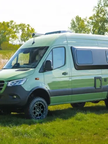 Grüner Westfalia James Cook 600 D Kastenwagen auf Mercedes Sprinter Basis steht auf einer Wiese vor Bäumen und einem See.