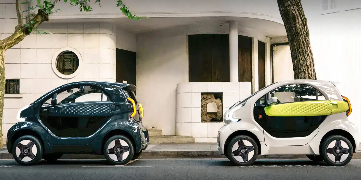 Zwei XEV YOYO PRO Stadtautos in verschiedenen Farben auf einer Straße vor einem Gebäudeeingang
