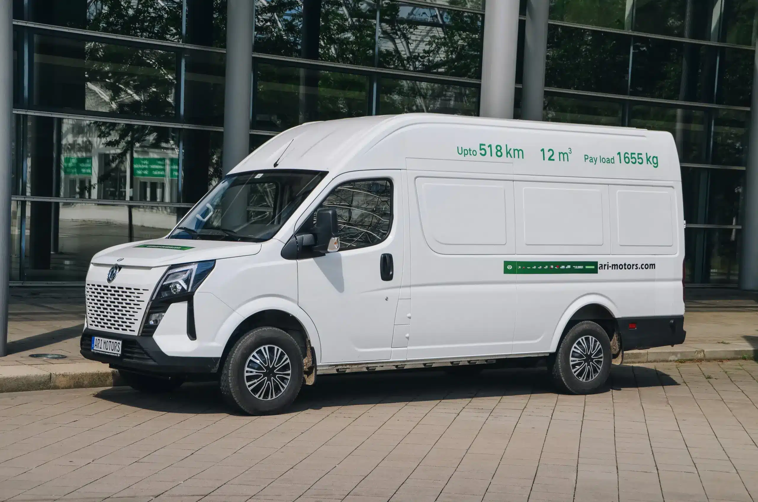 Seitenansicht eines weißen ARI 1710 Elektrotransporters vor einem modernen Gebäude, mit Herstelleraufschrift und technischen Angaben auf der Karosserie.