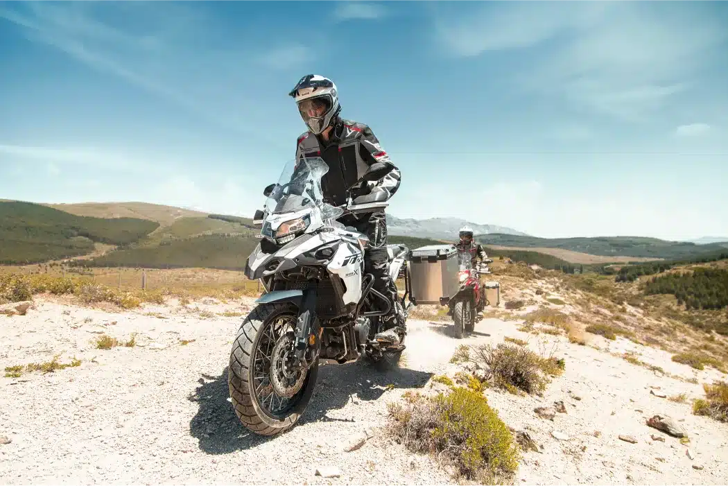 Benelli TRK 502 X Adventure-Bike wird von einem Fahrer auf einer staubigen Schotterstraße in bergiger Landschaft gesteuert.