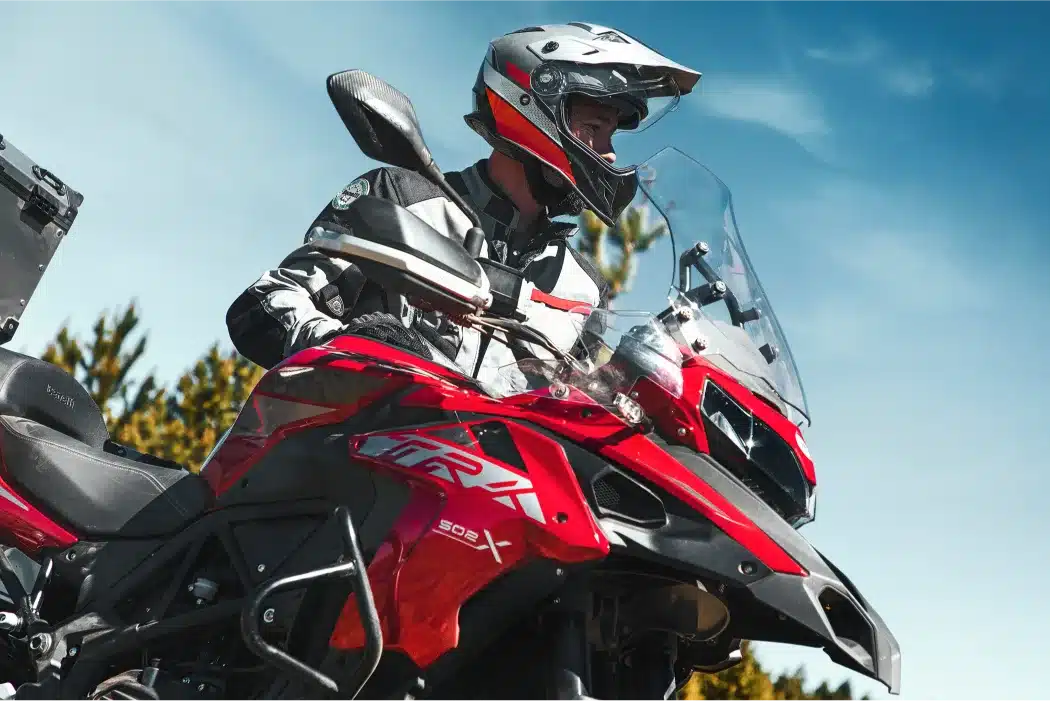 Motorradfahrer auf einer roten Benelli TRK 502 X mit Reiseausstattung und Helm vor blauem Himmel