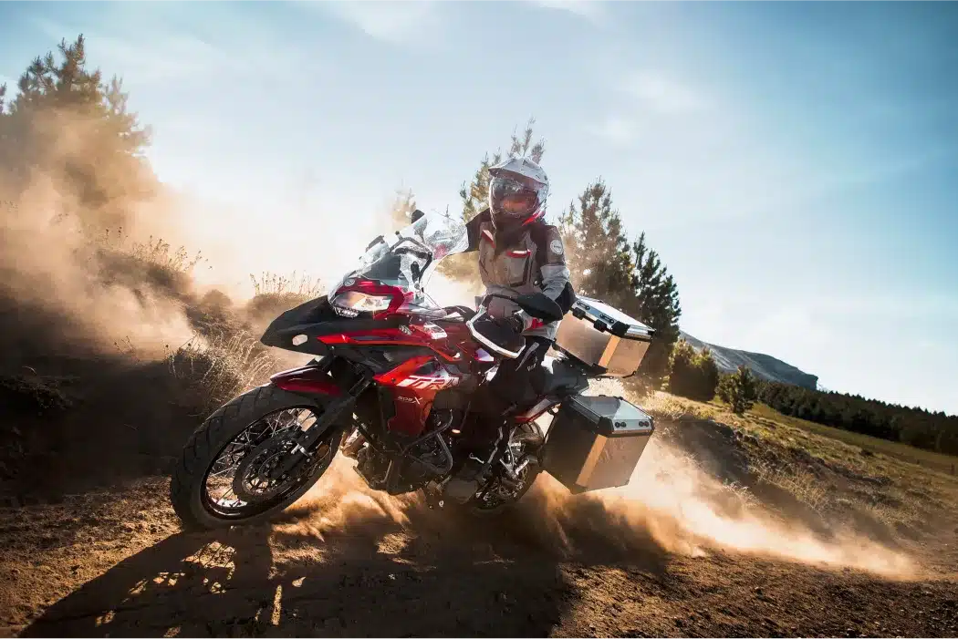 Abenteuer-Motorrad Benelli TRK 502 X mit Gepäckkoffern und Fahrer in voller Ausrüstung auf einer staubigen Strecke.