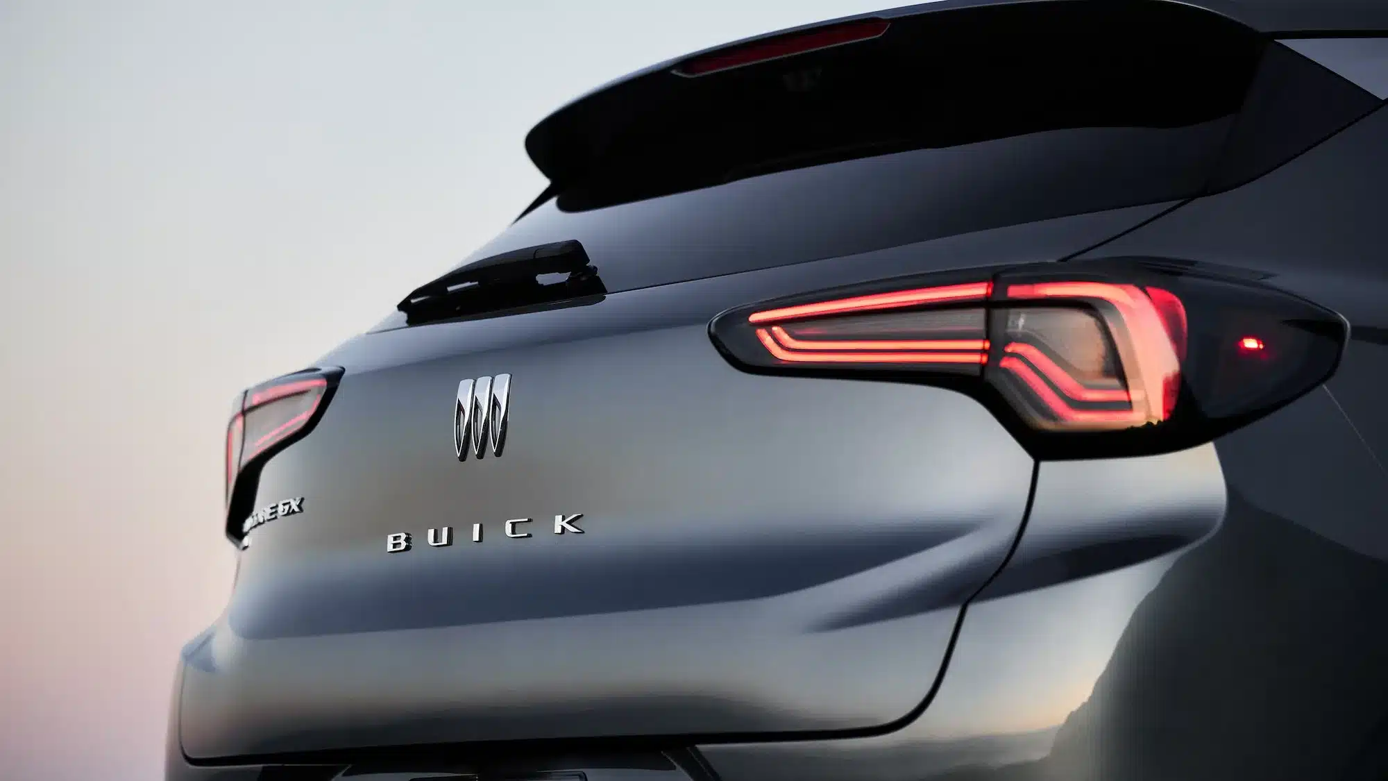 Rückansicht eines grauen 2026 Buick Encore GX mit beleuchteten LED-Rückleuchten und Buick-Logo.