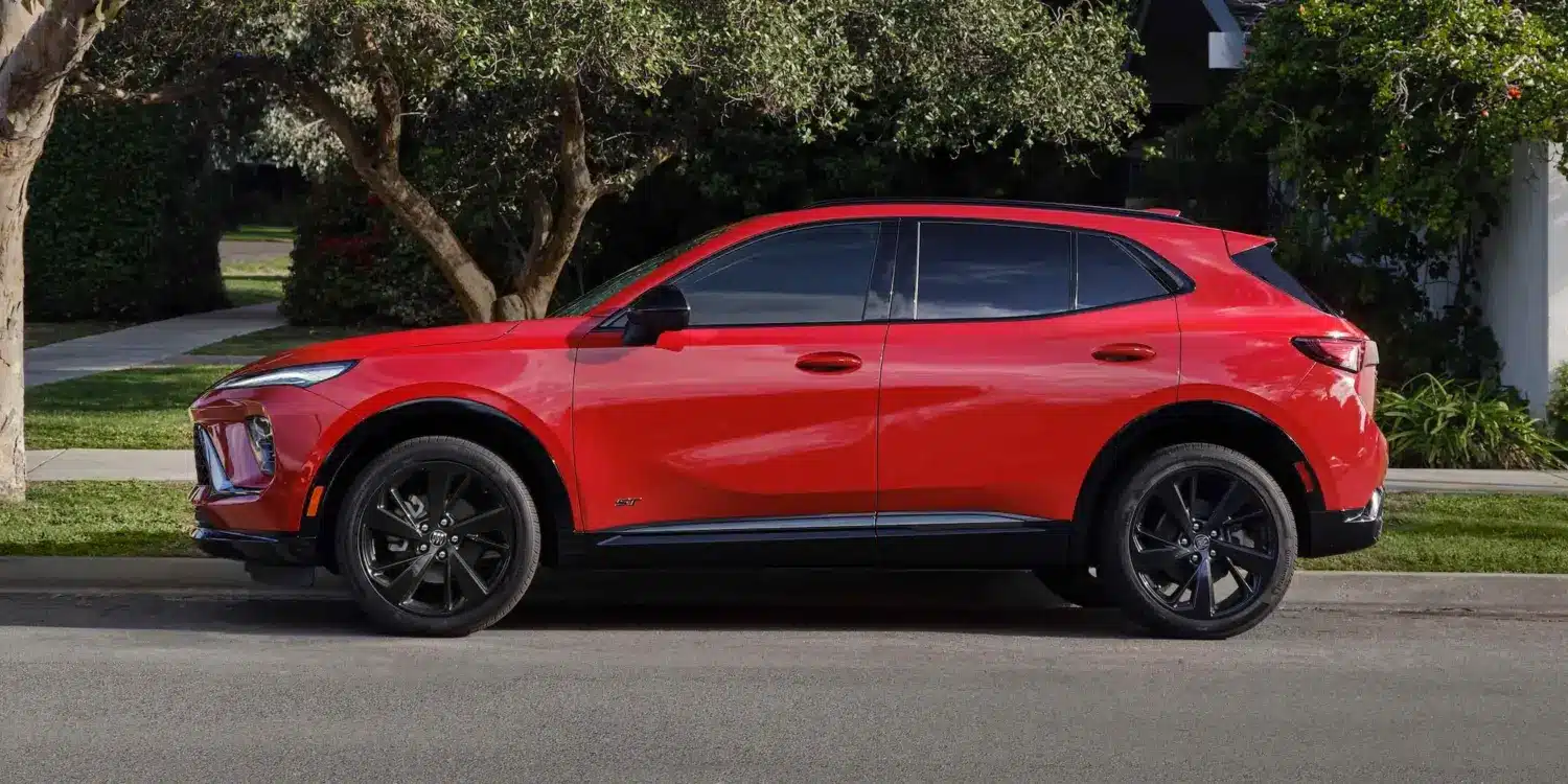 Buick Envision 2026 Sport Touring in Rot, Seitenansicht, geparkt am Straßenrand vor Bäumen