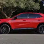 Buick Envision 2026 Sport Touring in Rot, Seitenansicht, geparkt am Straßenrand vor Bäumen