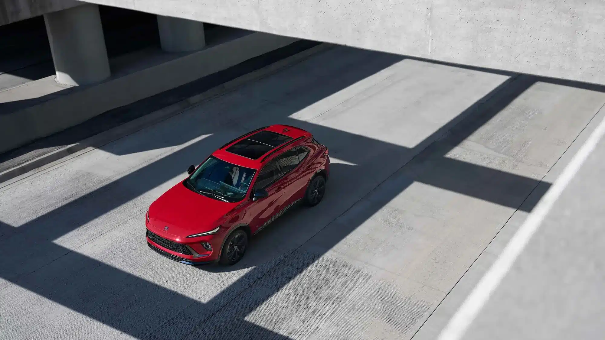 Roter Buick Envision 2026 SUV aus der Vogelperspektive, fahrend unter einer modernen Brücke.