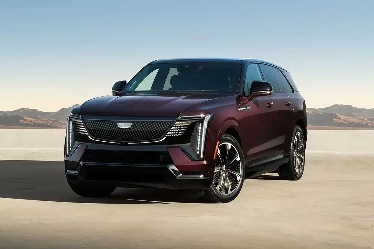 Frontansicht des Cadillac Escalade IQ in dunkler Lackierung auf einem offenen Platz vor Bergkulisse.
