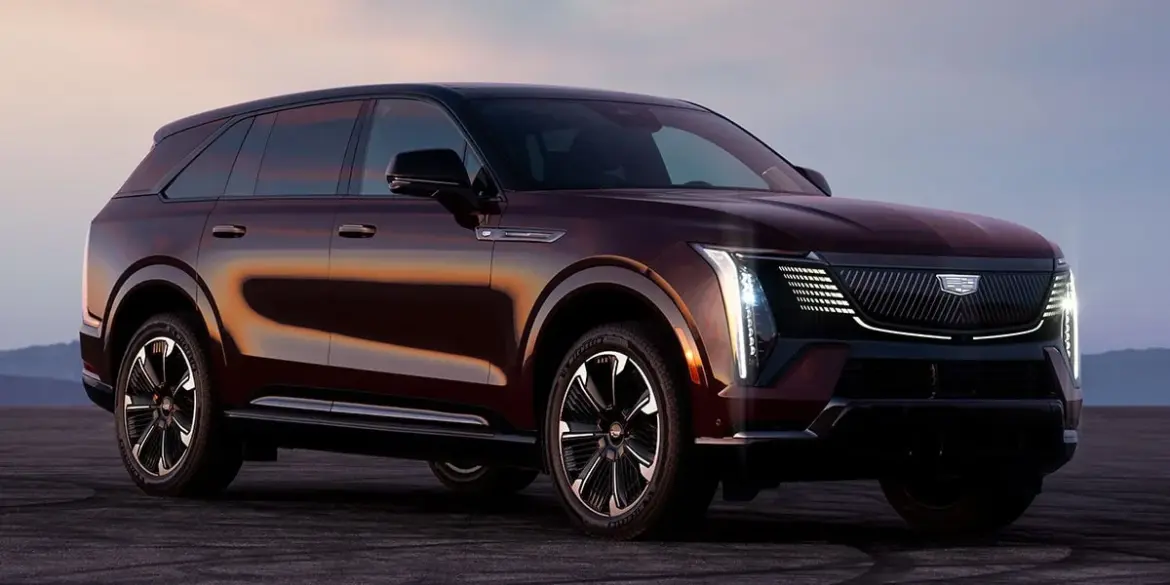 Cadillac Escalade IQ, großes elektrisches SUV in Dunkelrot auf offenem Asphalt bei Sonnenuntergang