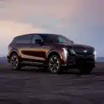 Cadillac Escalade IQ, großes elektrisches SUV in Dunkelrot auf offenem Asphalt bei Sonnenuntergang