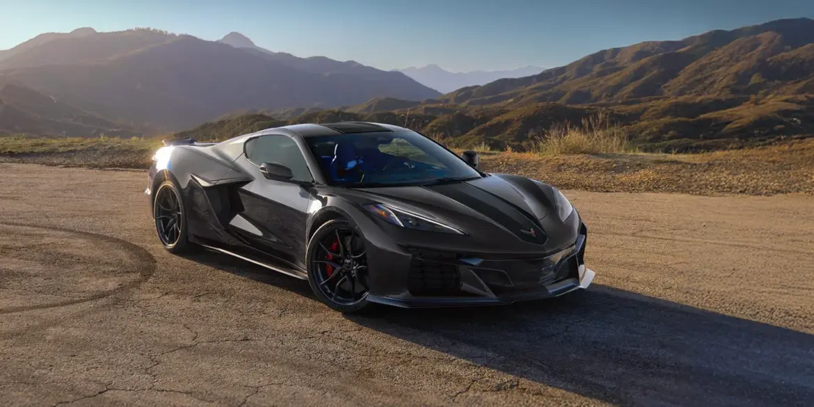 Schwarze Chevrolet Corvette Z06 vor Berglandschaft bei Sonnenaufgang auf einer Landstraße.