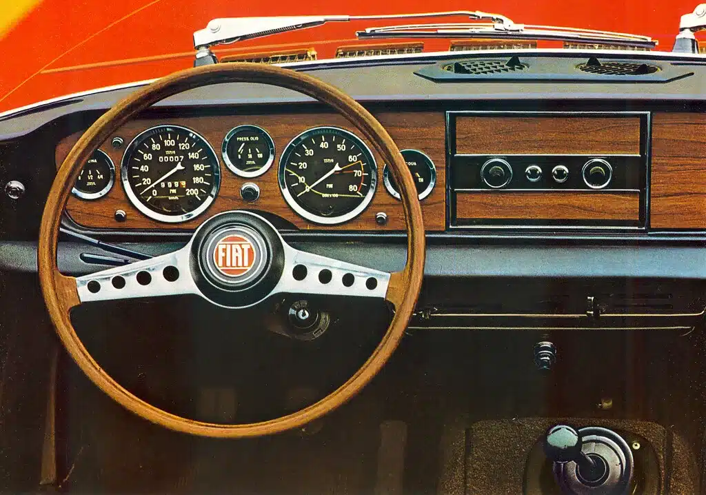 Armaturenbrett und Lenkrad eines Fiat 124 Sport Spider mit Holzzier und fünf Rundinstrumenten.