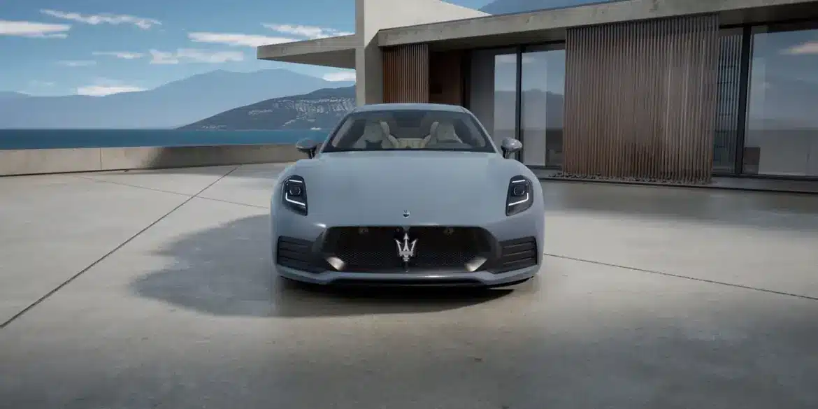 Frontansicht des Maserati GranTurismo Folgore in Hellgrau vor moderner Architektur und Meereshintergrund.