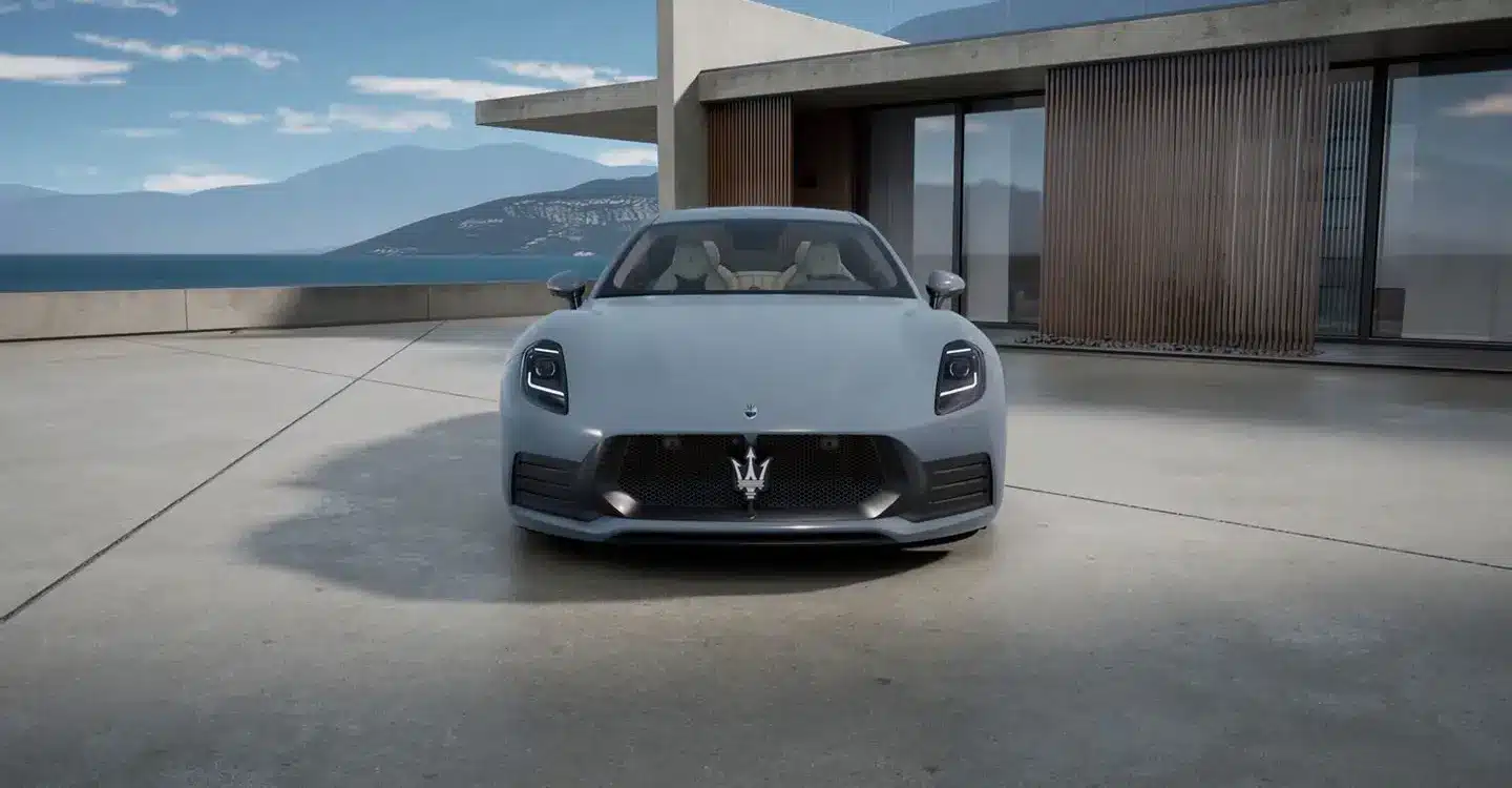 Frontansicht des Maserati GranTurismo Folgore in Hellgrau vor moderner Architektur und Meereshintergrund.
