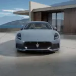 Frontansicht des Maserati GranTurismo Folgore in Hellgrau vor moderner Architektur und Meereshintergrund.