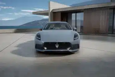 Frontansicht des Maserati GranTurismo Folgore in Hellgrau vor moderner Architektur und Meereshintergrund.