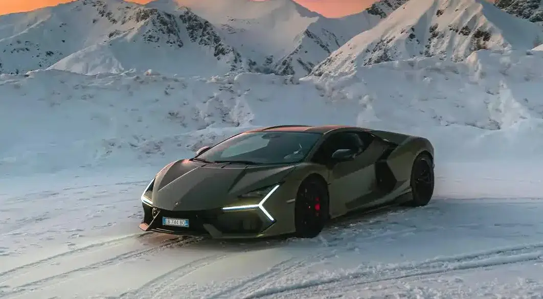 Lamborghini Revuelto steht auf Schnee vor schneebedeckten Bergen bei Sonnenuntergang.