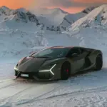 Lamborghini Revuelto steht auf Schnee vor schneebedeckten Bergen bei Sonnenuntergang.