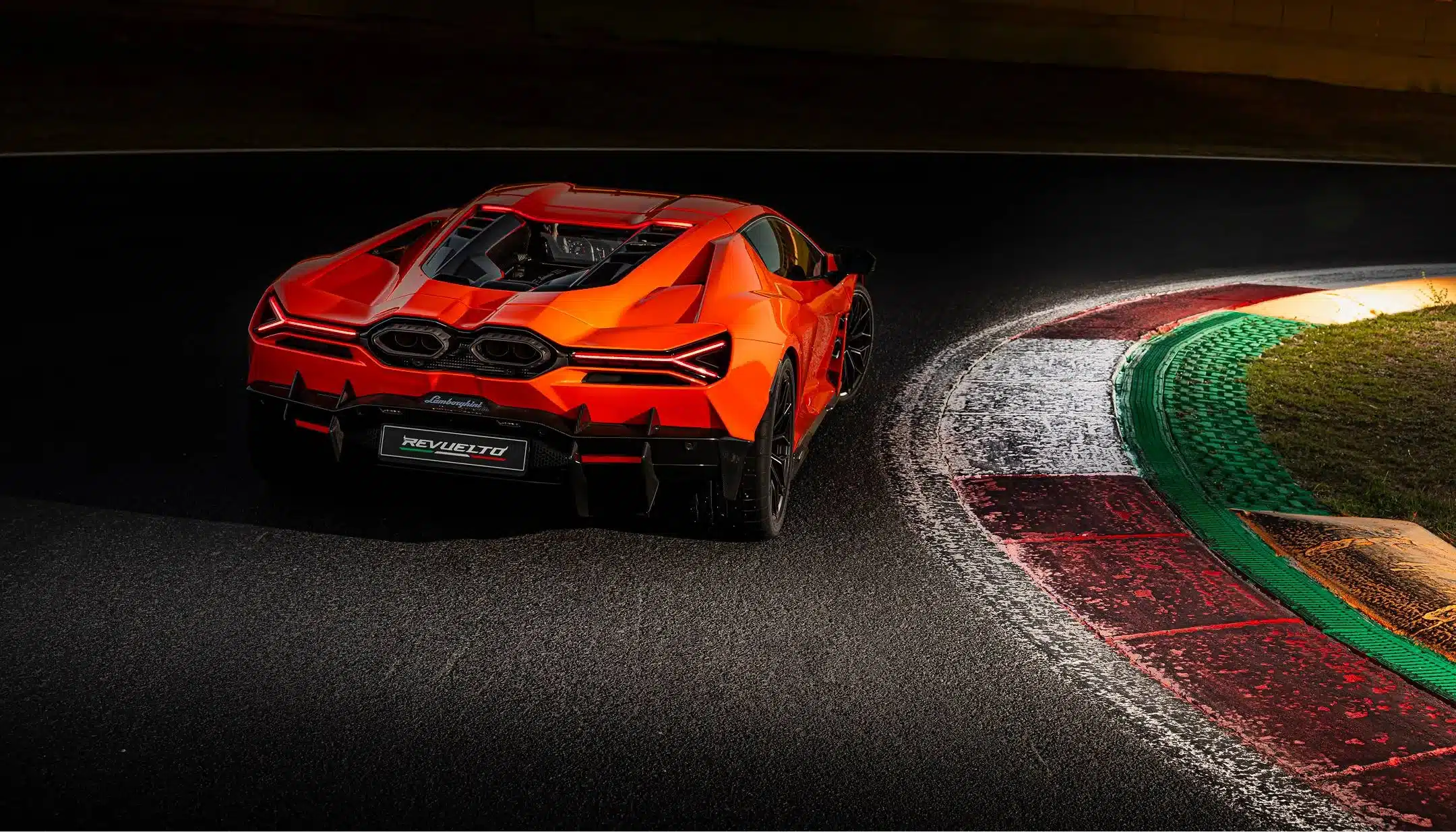 Heckansicht eines orangefarbenen Lamborghini Revuelto auf einer Rennstrecke mit aktivem Heckflügel.