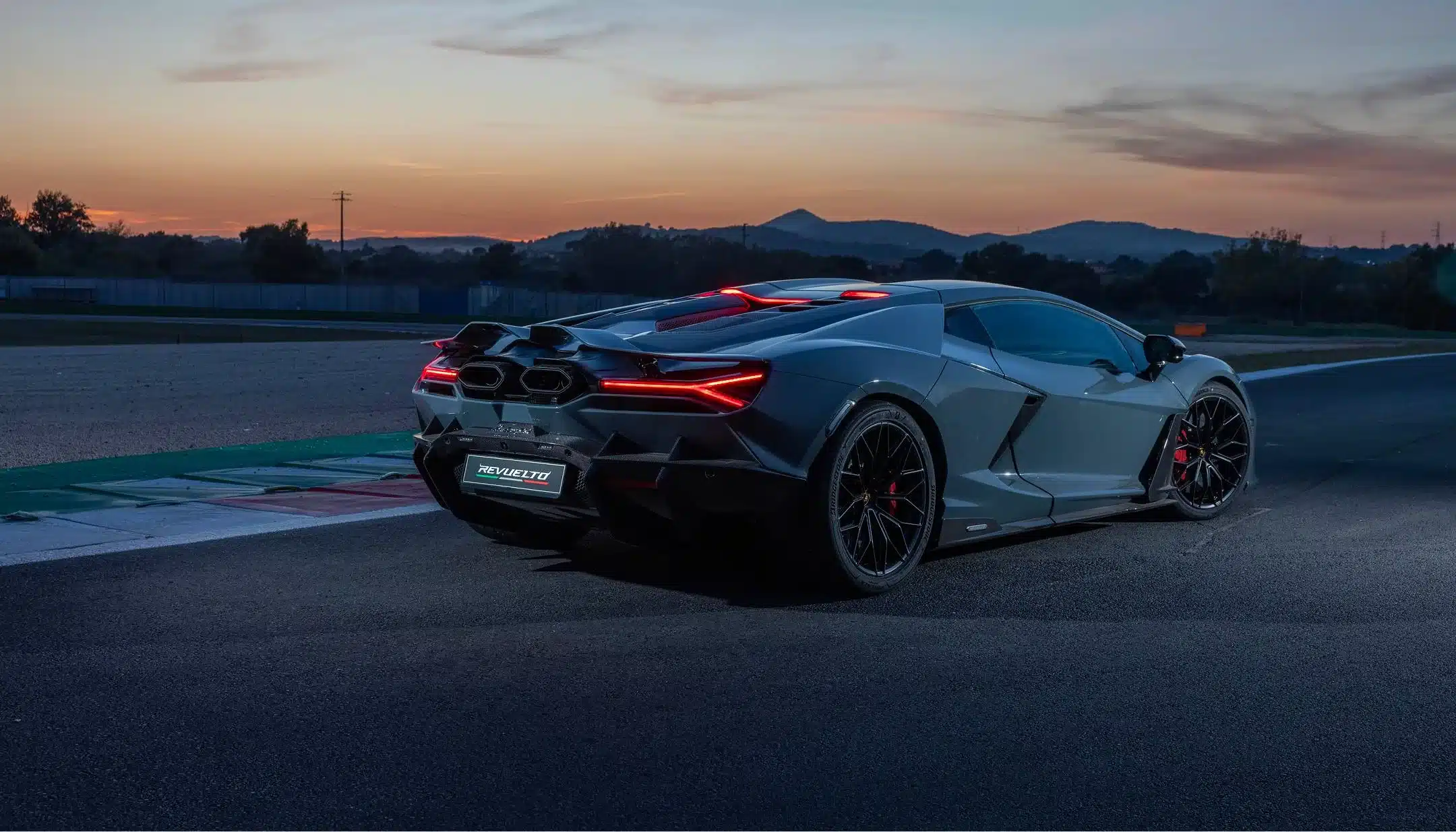 Heckansicht eines Lamborghini Revuelto auf einer Rennstrecke bei Dämmerung, aktive Aerodynamik erkennbar.