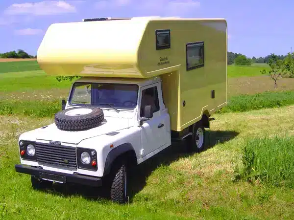 Gelber Offroad-Camper auf Landrover-Basis steht auf einer Wiese, ideal für unabhängige Reisen.