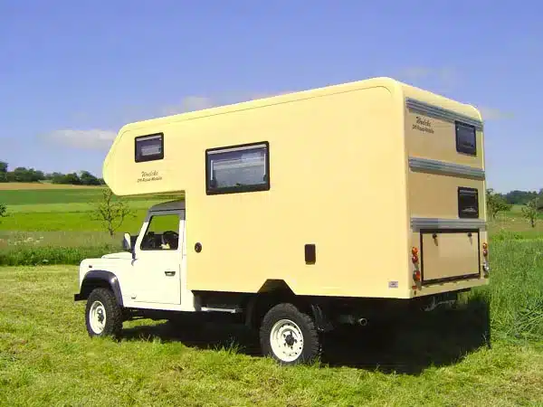 Landrover Offroad-Camper mit gelbem GFK-Wohnaufbau auf einer Wiese