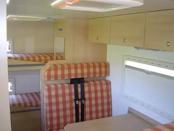 Innenansicht des Landrover Offroad-Campers mit Sitzbank, Esstisch, Schränken und Etagenbetten.