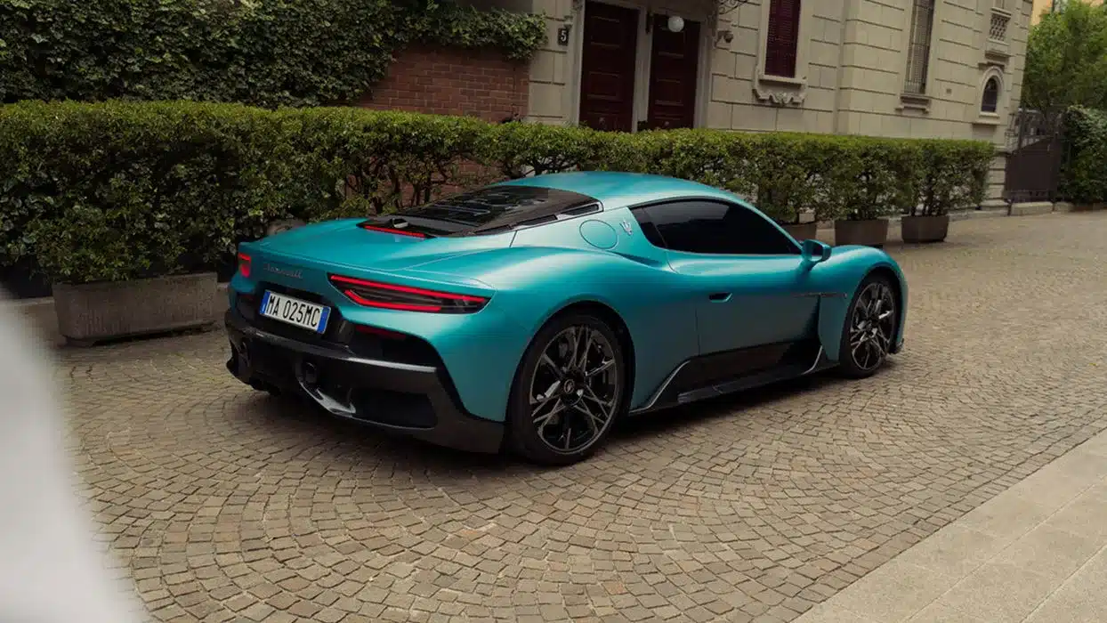 Maserati MCPura Coupé in Türkis, seitliche Heckansicht auf einem gepflasterten Platz vor einer Villa.