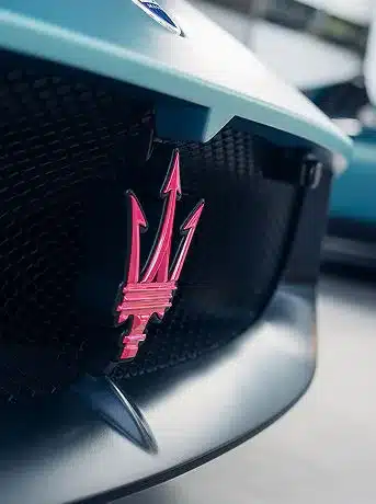 Detailaufnahme des pinkfarbenen Maserati-Tridents an der Front des MCPura Supersportwagens.
