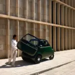Grüner Microlino mit geöffneter Fronttür, eine Person steigt aus, moderne Gebäudewand im Hintergrund.