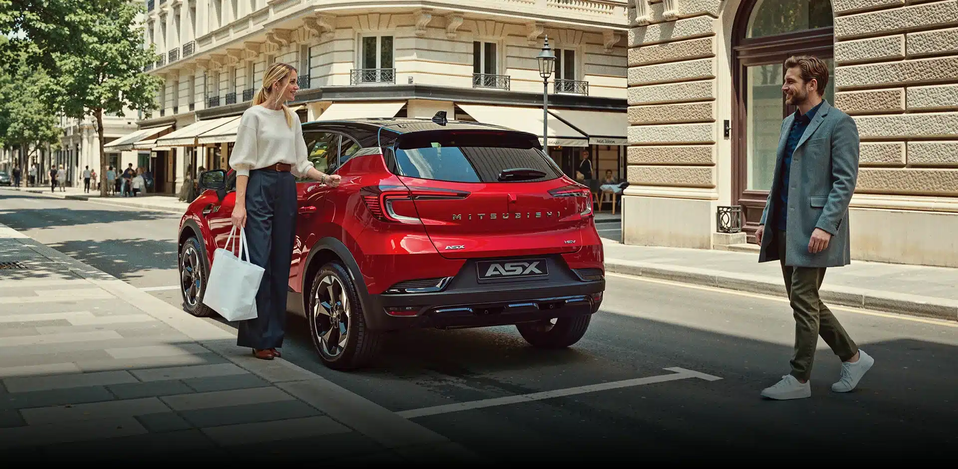 Roter Mitsubishi ASX parkt am Straßenrand in einer europäischen Stadt, eine Frau steht neben dem Fahrzeug, ein Mann nähert sich.