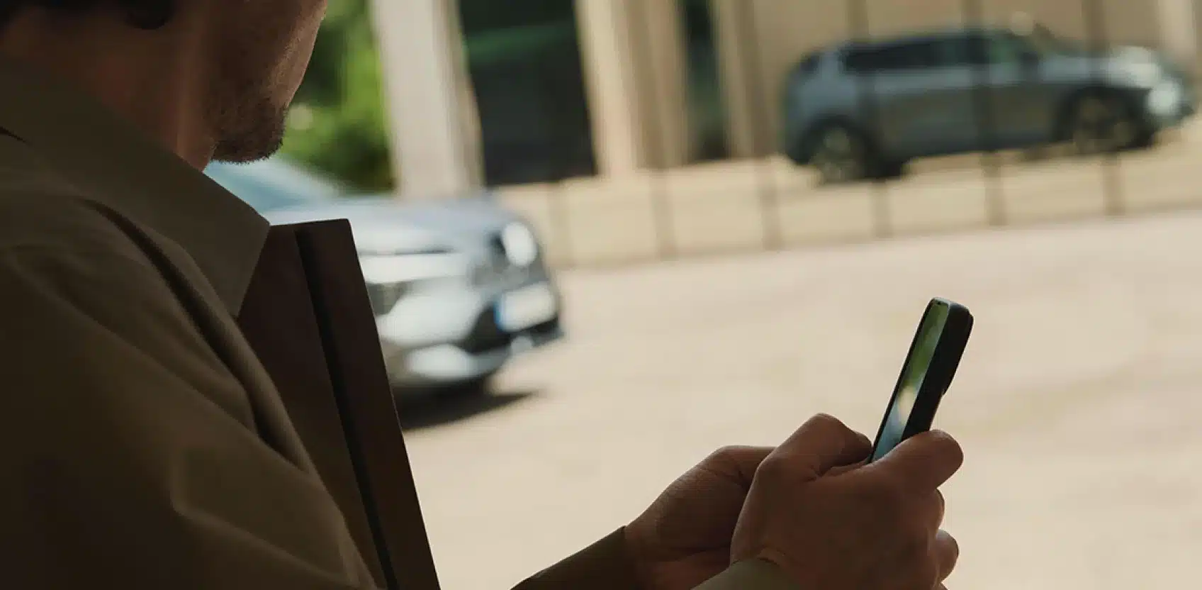 Mann bedient eine Smartphone-App, während im Hintergrund ein Mitsubishi Eclipse Cross Elektro-SUV steht
