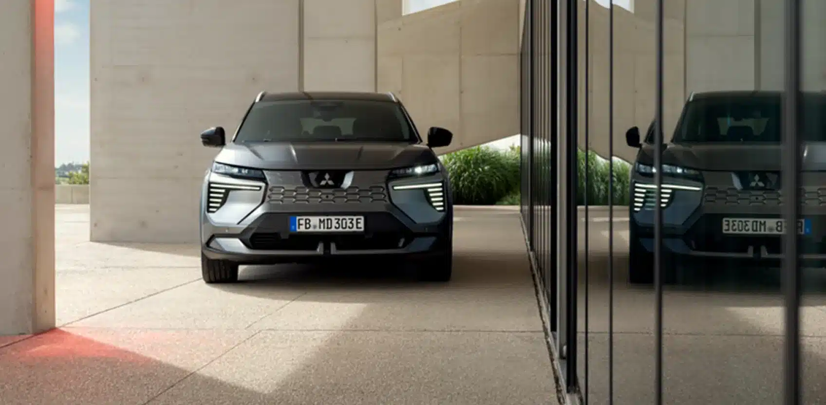 Frontansicht des Mitsubishi Eclipse Cross als vollelektrischer SUV vor moderner Architektur.