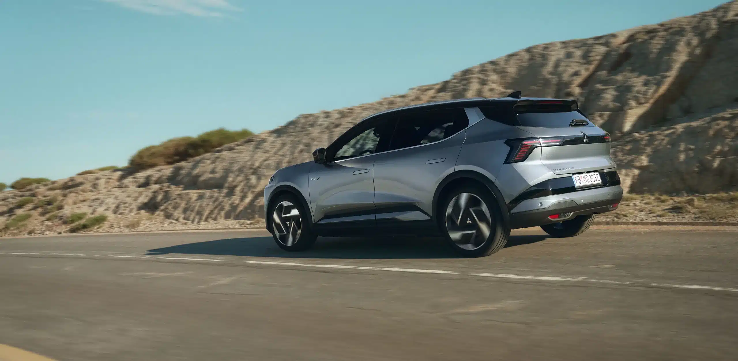 Mitsubishi Eclipse Cross Elektro-SUV fährt auf einer Straße entlang felsiger Landschaft.