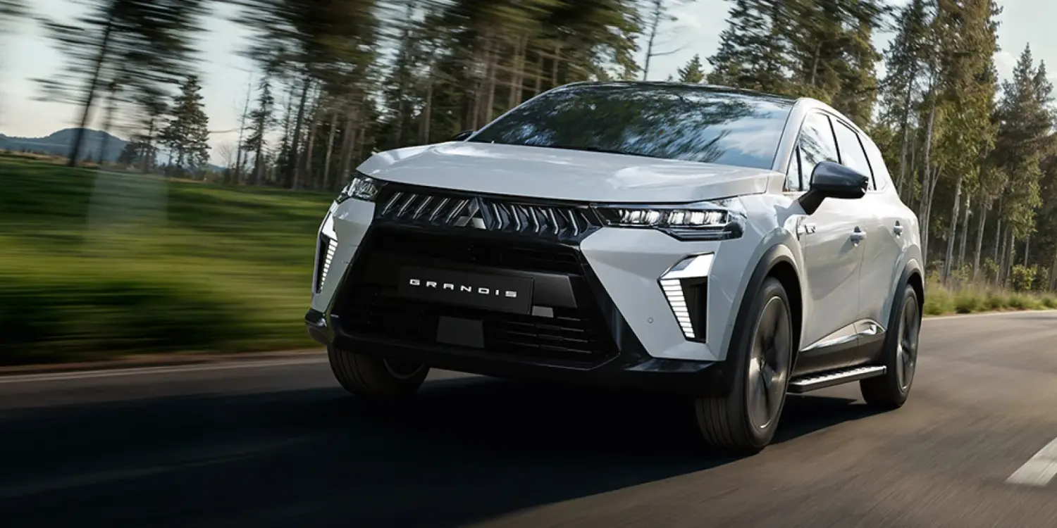 Der neue Mitsubishi Grandis Hybrid-SUV fährt auf einer von Bäumen gesäumten Landstraße.