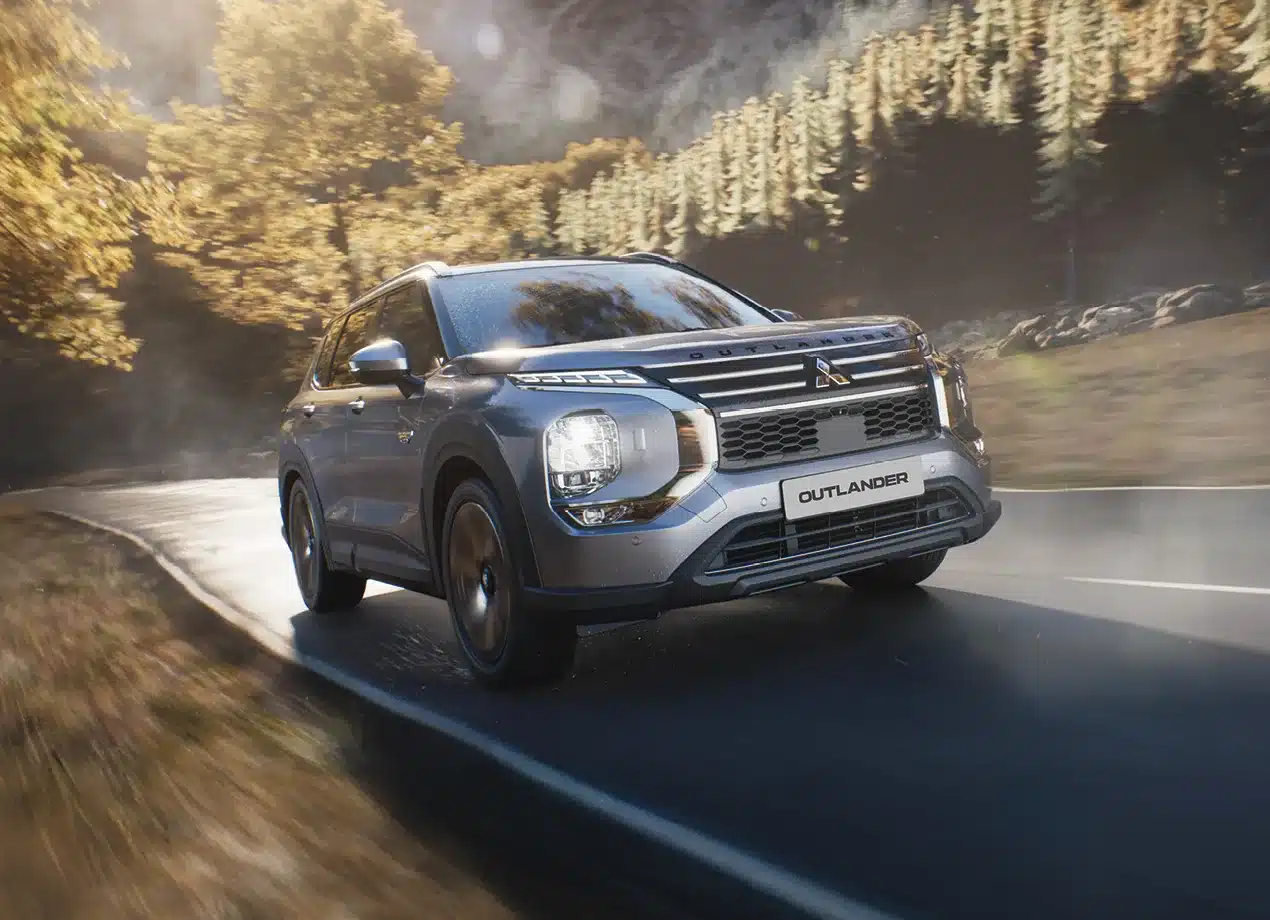 Mitsubishi Outlander PHEV fährt dynamisch auf einer herbstlichen Straße durch den Wald.